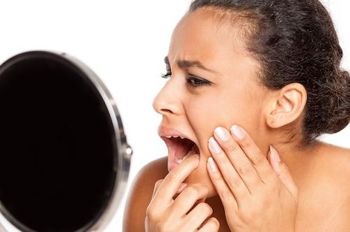 woman looking at tooth in a mirror during an emergency