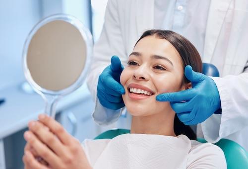 woman in dental chair smiling into a dental mirror