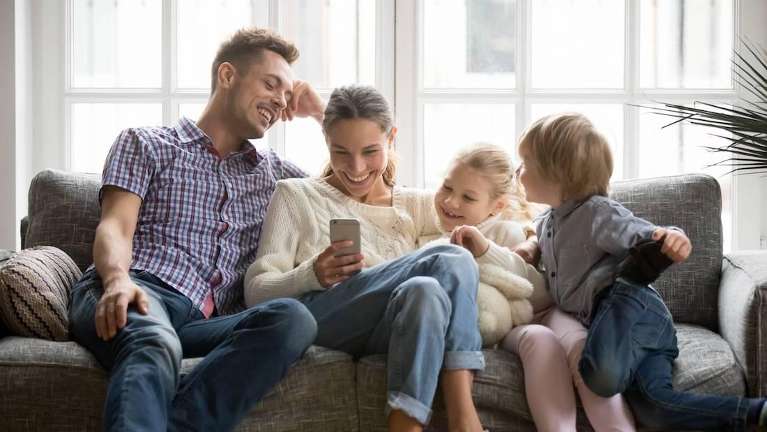 Dad, mom, and two young children looking at cell phone on couch